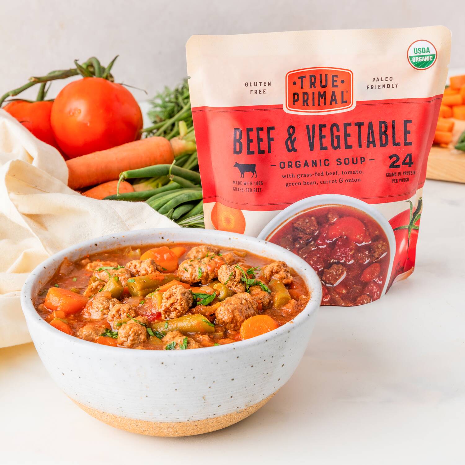 Beef and Vegetable Soup in bowl in front of fresh veggies and pouch