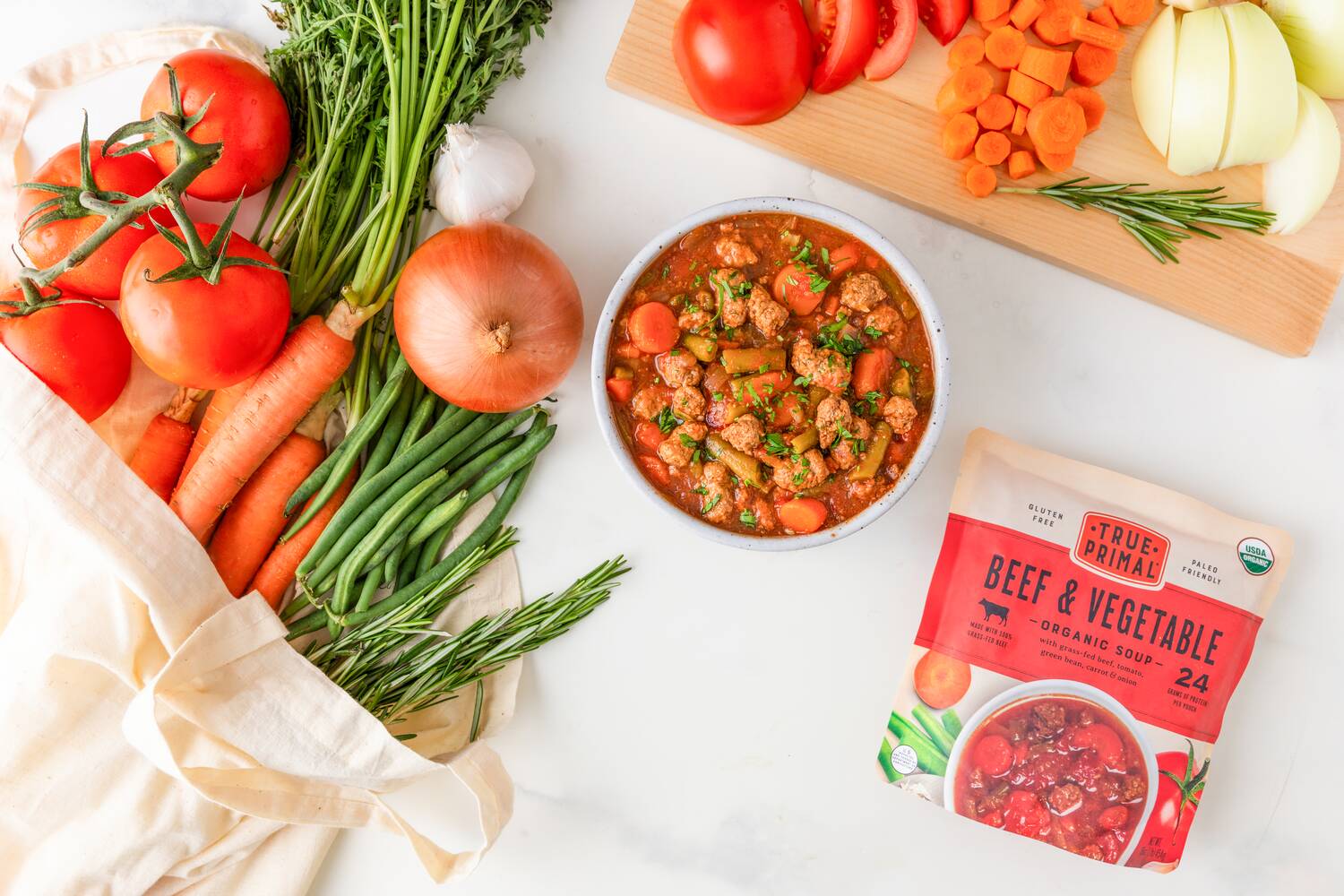 Beef and Vegetable Soup in bowl next to fresh veggies and pouch