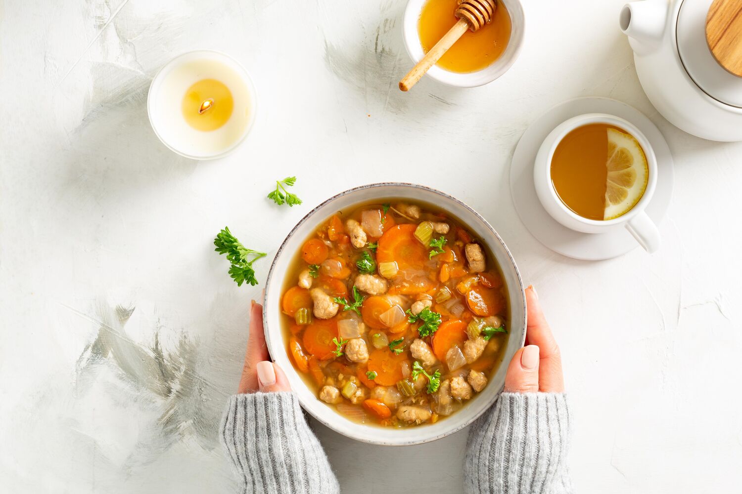 Roasted Chicken Soup on table with honey lemon tea and hands holding the bowl