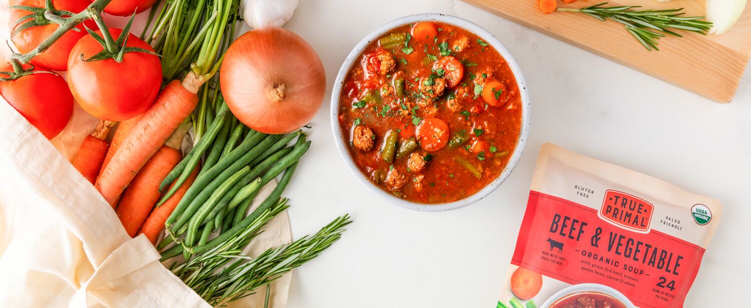 True Primal Beef & Vegetable Organic Soup in bowl next to pouch and vegetables
