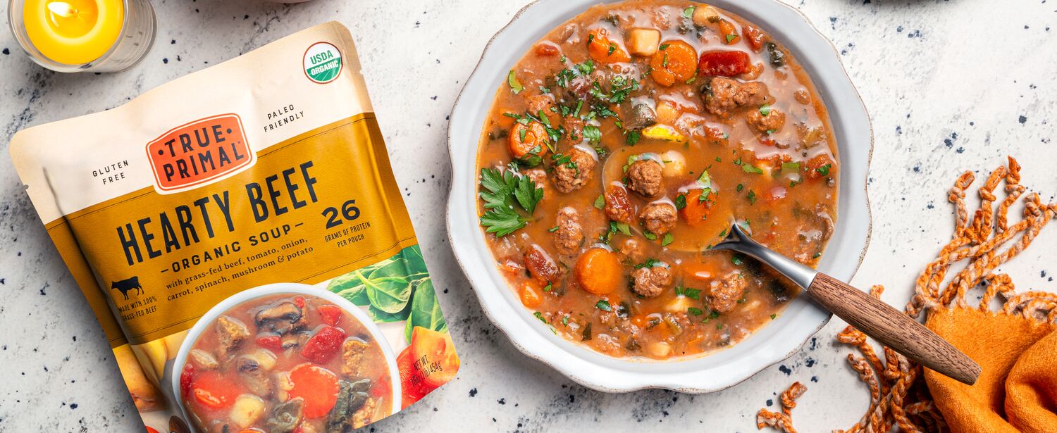 True Primal Hearty Beef Organic Soup in bowl next to pouch and crackers