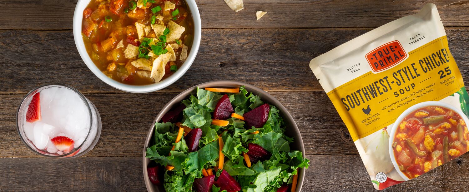 True Primal Southwest-Style Chicken Soup in bowl next to pouch and salad