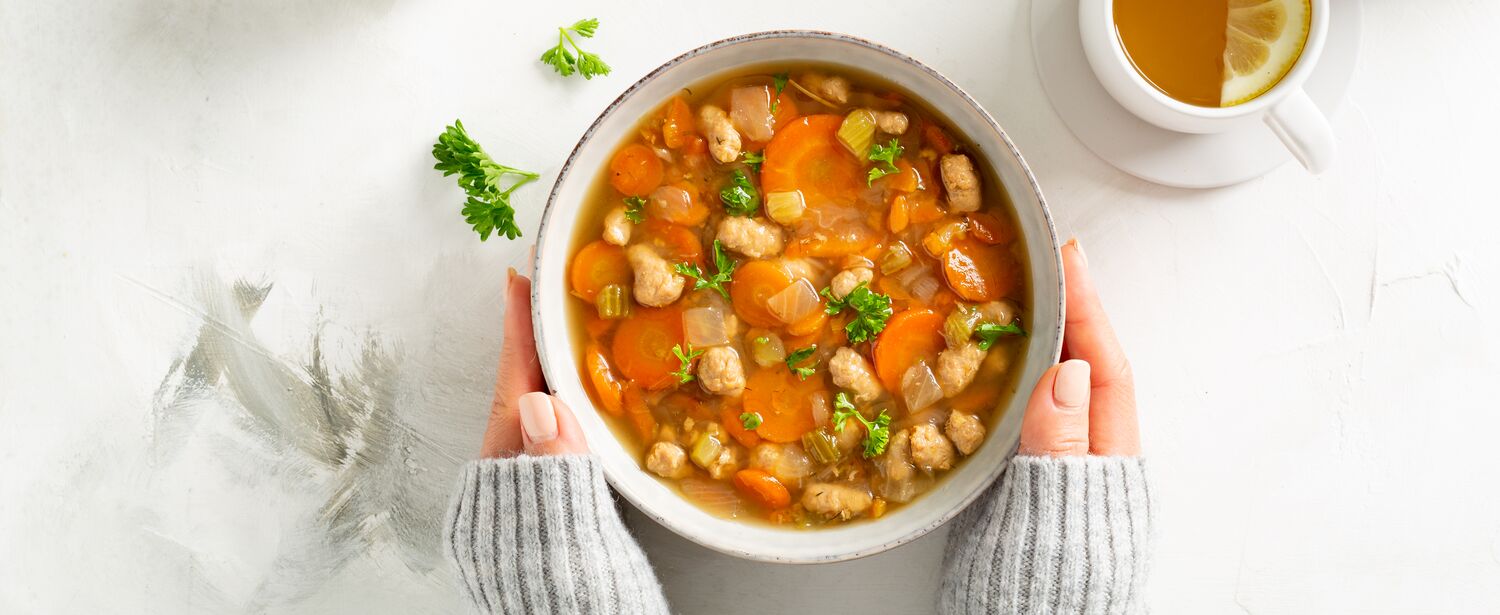 hands holding True Primal Roasted Chicken Soup in a bowl