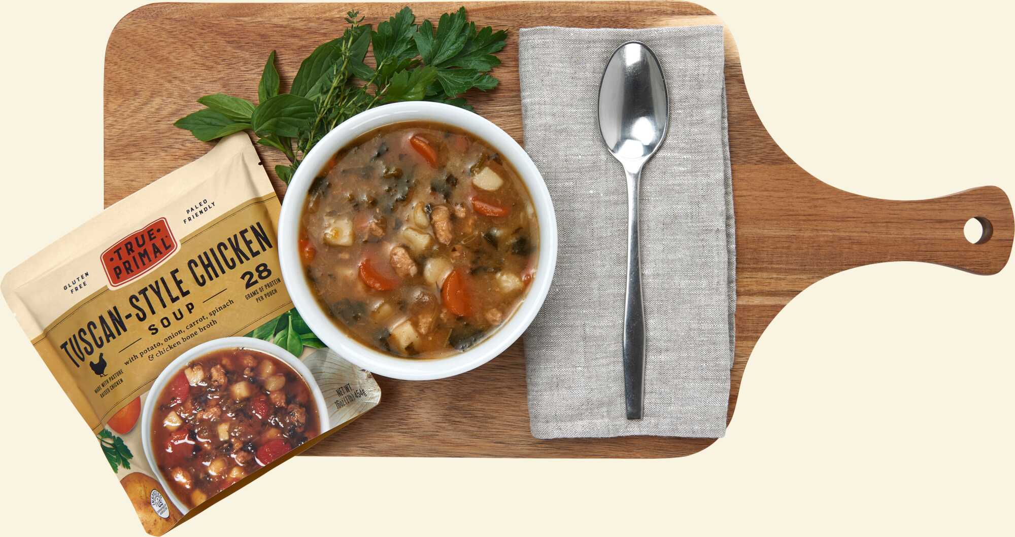 True Primal Tuscan-Style Chicken Soup on cutting board with spoon