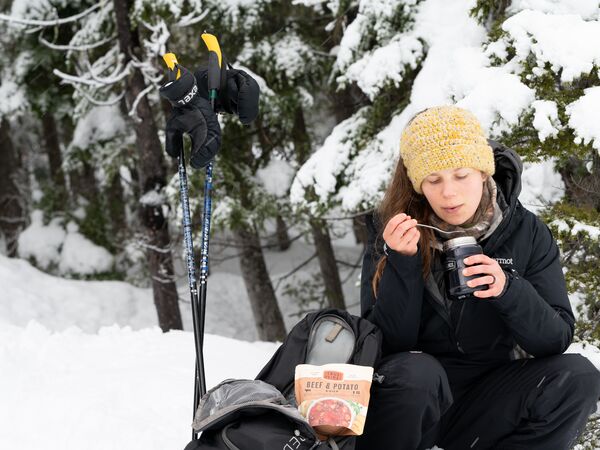 woman eating soup out of a thermos in the snow