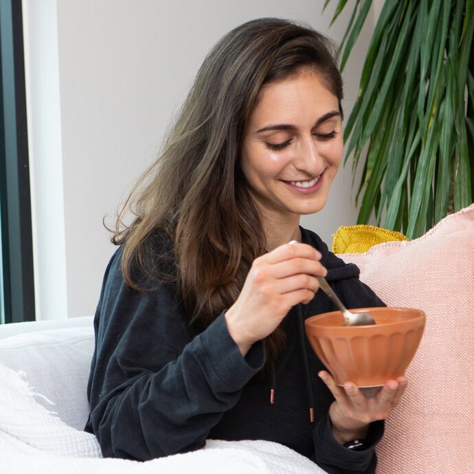 woman on couch with a pillow and bowl and spoon smiling