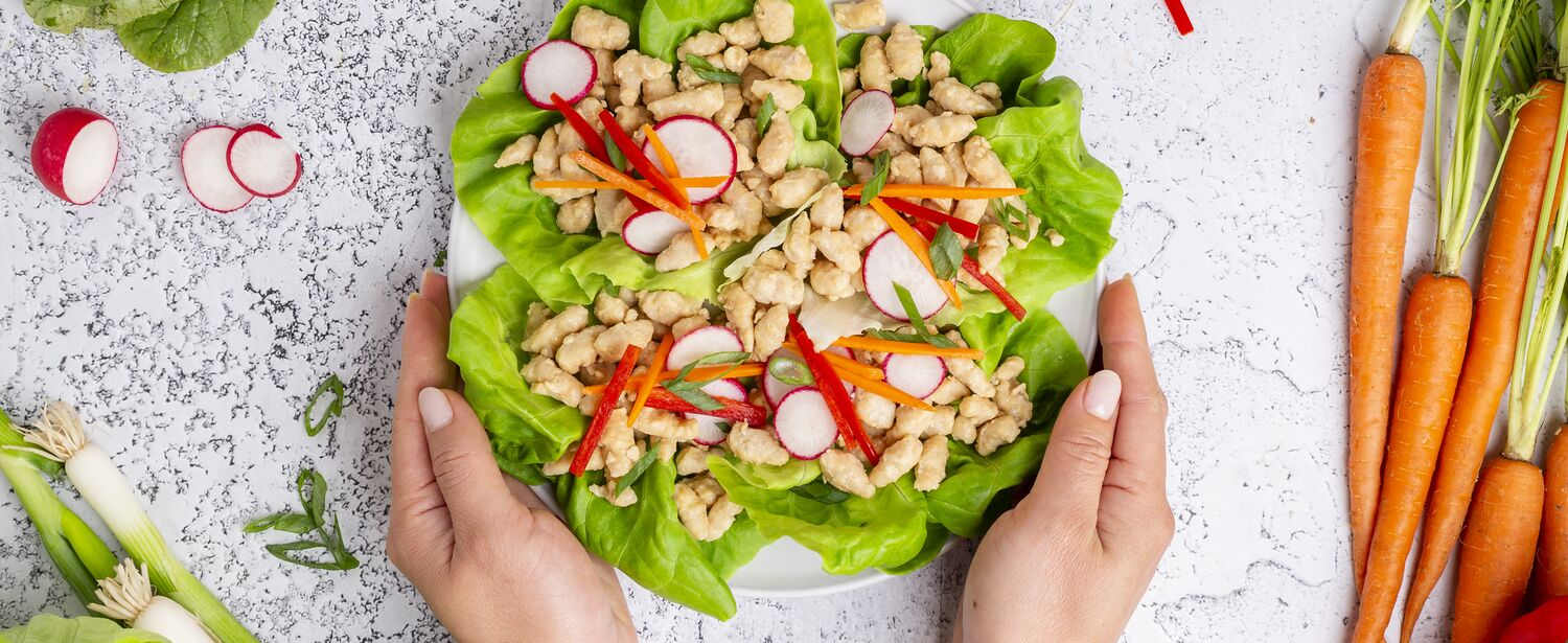 Hands holding plate of True Primal Pastured Chicken Mini Meatballs in lettuce cups on plate