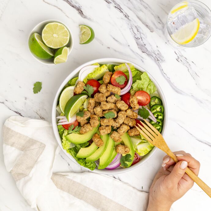 True Primal Grass-fed Beef Mini Meatballs on salad in bowl with hand and fork