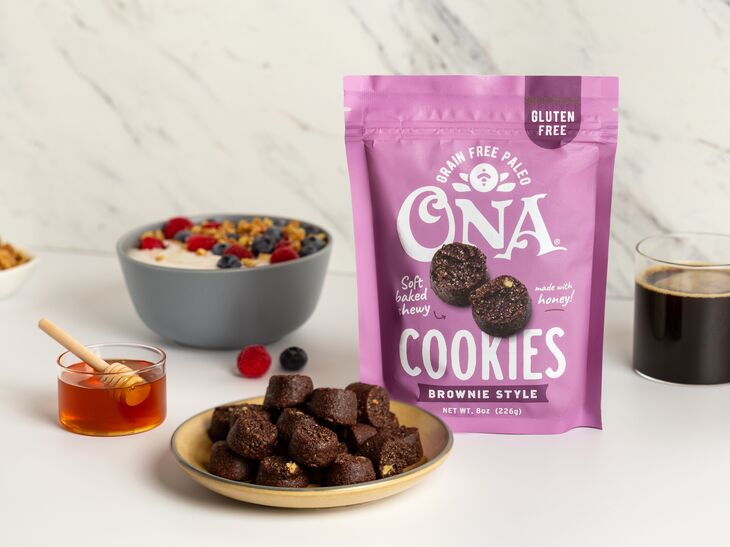 Ona Brownie Style Cookies on a plate and in a pouch, next to coffee, a bowl of cereal, and honey