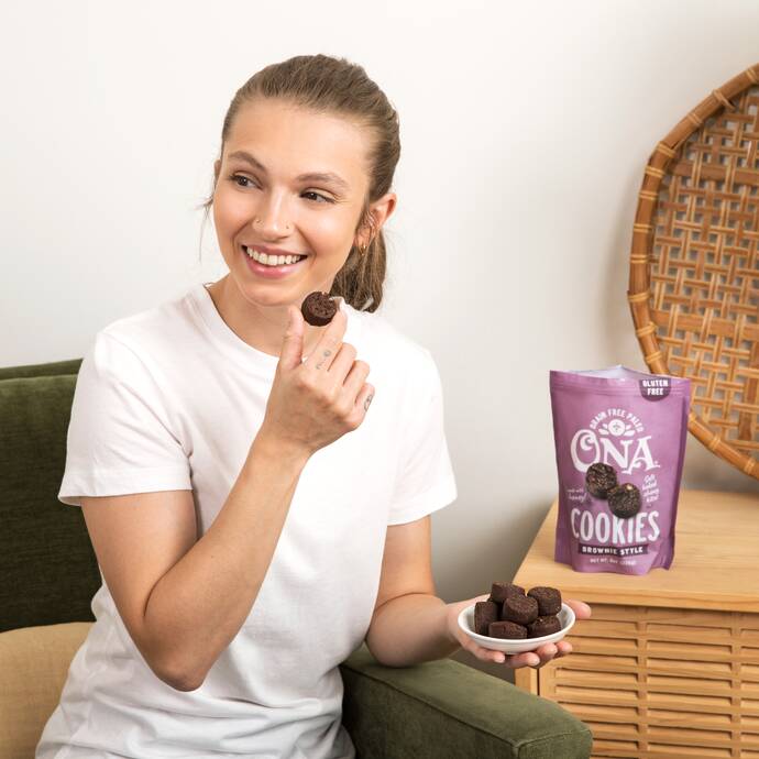 smiling woman on a couch eating Ona Brownie Style Cookies