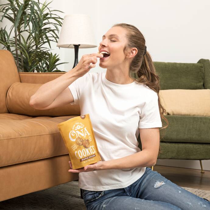 smiling woman on a couch eating Ona Ona Maple Pecan Cookies