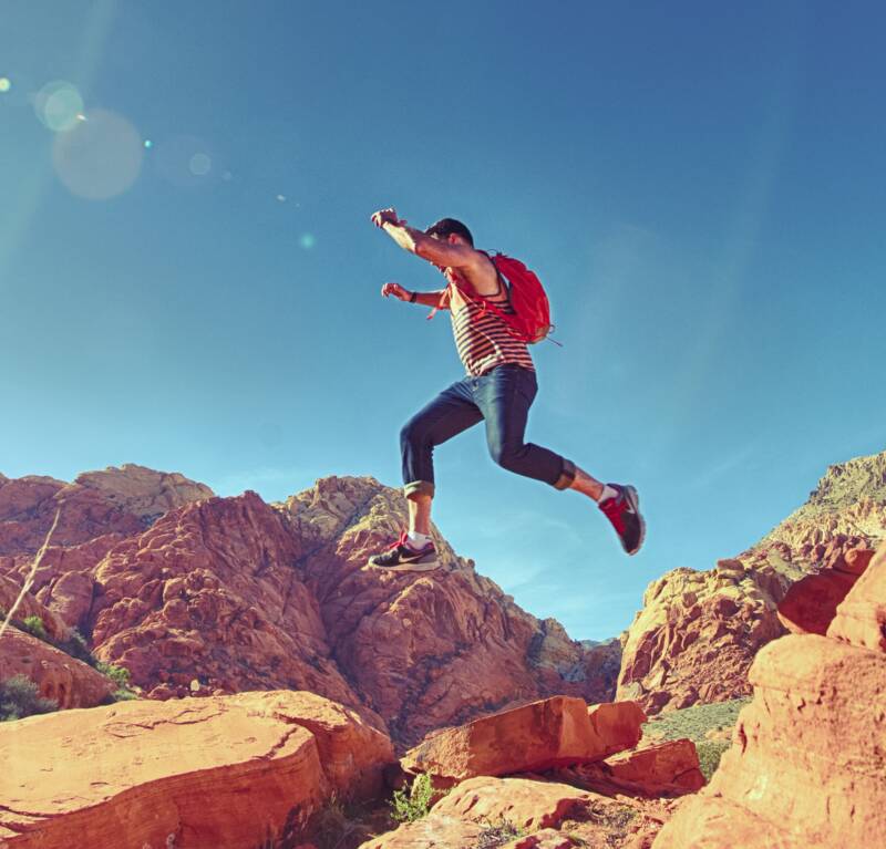 man in mountainous landscape jumping from one large rock to another