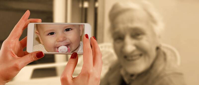 older adult woman next to phone showing image of a baby with a similar pose
