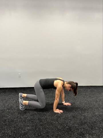 Woman in a bear crawl, on hands and toes with knees bent and hovering above the ground- opposite hand and foot moving simultaneously.